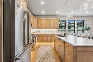 Condo Model Example. Kitchen featuring an island with sink, sink, premium appliances, hanging light fixtures, and light brown cabinets