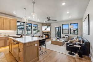 Condo Model Example. Kitchen with a stone fireplace, sink, decorative light fixtures, a center island with sink, and light wood-type flooring