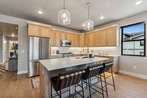 Condo Model Example. Kitchen with light brown cabinetry, premium appliances, sink, and a center island with sink