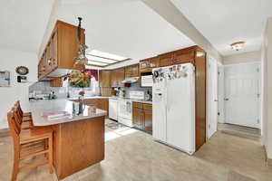 Kitchen featuring a kitchen bar, a skylight, kitchen peninsula, white appliances, and backsplash