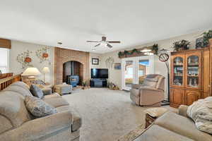 Living room featuring a wood stove, light colored carpet, and ceiling fan