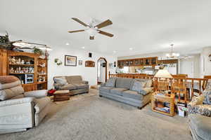 Living room featuring ceiling fan with notable chandelier and carpet flooring