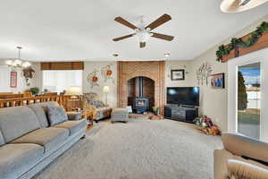 Living room with ceiling fan with notable chandelier, carpet floors, and a wood stove