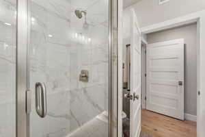 Bathroom with hardwood / wood-style flooring, toilet, and a shower with door