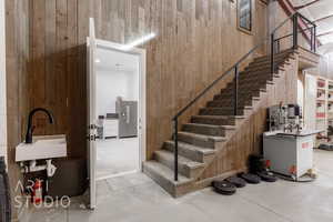 Staircase featuring wooden walls, sink, and concrete floors