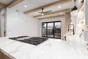 Kitchen featuring beamed ceiling, ceiling fan, light stone countertops, and gas stovetop