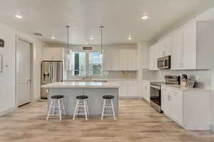 Kitchen featuring a breakfast bar, white cabinetry, a center island, appliances with stainless steel finishes, and decorative backsplash