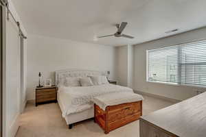 Carpeted bedroom with a barn door and ceiling fan