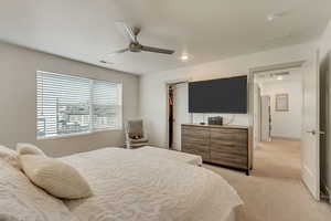 Bedroom featuring a spacious closet, light colored carpet, ceiling fan, and a closet