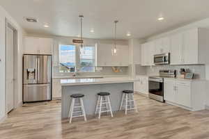 Kitchen featuring a kitchen bar, sink, a kitchen island, stainless steel appliances, and white cabinets