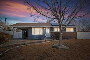 Ranch-style house featuring roof mounted solar panels, a carport, concrete driveway, a gate, and brick siding