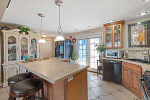 Kitchen featuring glass insert cabinets, a sink, stainless steel appliances, light countertops, and backsplash