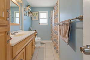 Full bath featuring baseboards, a shower with shower curtain, toilet, tile patterned flooring, and vanity