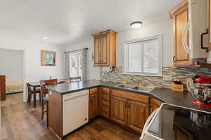 Kitchen featuring dark hardwood / wood-style floors, tasteful backsplash, sink, kitchen peninsula, and white appliances