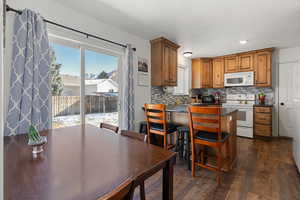 Kitchen featuring white appliances, dark hardwood / wood-style flooring, a kitchen breakfast bar, and decorative backsplash