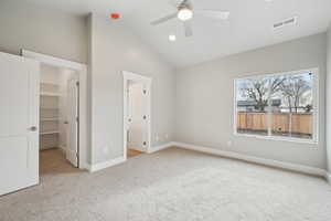 Unfurnished bedroom featuring ceiling fan, vaulted ceiling, a walk in closet, light colored carpet, and a closet