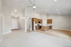 Kitchen with high vaulted ceiling, a center island with sink, light colored carpet, stainless steel appliances, and ceiling fan with notable chandelier