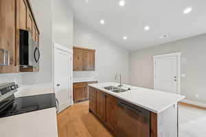 Kitchen featuring sink, high vaulted ceiling, light wood-type flooring, stainless steel appliances, and a kitchen island with sink