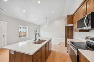 Kitchen with lofted ceiling, sink, light wood-type flooring, appliances with stainless steel finishes, and an island with sink