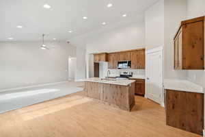 Kitchen featuring high vaulted ceiling, a center island with sink, light hardwood / wood-style flooring, ceiling fan, and stainless steel appliances