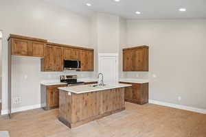 Kitchen with high vaulted ceiling, an island with sink, sink, stainless steel appliances, and light wood-type flooring