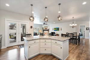 Kitchen with white cabinetry, wood-type flooring, pendant lighting, ceiling fan, and light stone countertops