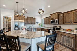 Kitchen with a breakfast bar area, light stone counters, decorative light fixtures, a kitchen island, and stainless steel appliances