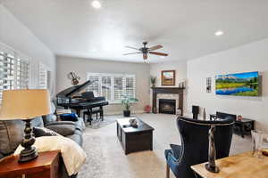 Living room featuring a fireplace, light colored carpet, and ceiling fan