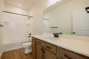 Full bathroom with hardwood / wood-style flooring, vanity, tiled shower / bath combo, and toilet