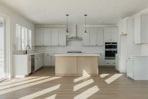 Kitchen with a kitchen island, white cabinets, double oven, and wall chimney exhaust hood