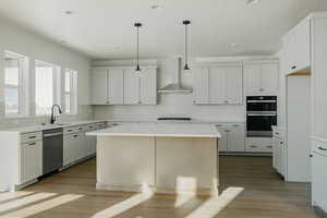 Kitchen featuring white cabinetry, wall chimney range hood, a center island, and appliances with stainless steel finishes