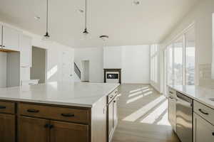 Kitchen with white cabinetry, decorative light fixtures, stainless steel dishwasher, light stone countertops, and light hardwood / wood-style floors