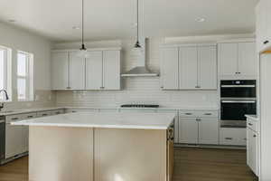 Kitchen with white cabinetry, hanging light fixtures, double oven, light stone countertops, and a kitchen island