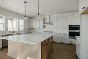 Kitchen with wall chimney exhaust hood, sink, white cabinetry, a center island, and dishwasher