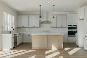 Kitchen with pendant lighting, multiple ovens, wall chimney exhaust hood, and a kitchen island