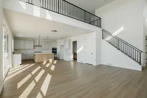 Unfurnished living room with a towering ceiling, sink, and light wood-type flooring