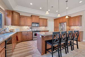 Kitchen featuring a kitchen island, pendant lighting, sink, a tray ceiling, and stainless steel appliances