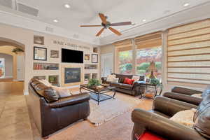 Living room featuring a tiled fireplace, light tile patterned floors, a raised ceiling, and ceiling fan