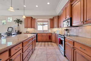 Kitchen with pendant lighting, tasteful backsplash, light tile patterned floors, light stone counters, and stainless steel appliances