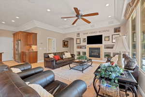 Living room featuring light tile patterned flooring, built in features, a tiled fireplace, ceiling fan, and crown molding