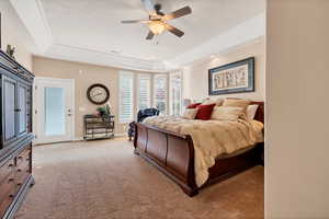 Bedroom featuring access to exterior, a tray ceiling, light colored carpet, and ceiling fan