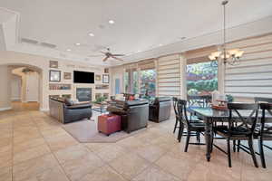 Living room featuring a tray ceiling, ceiling fan with notable chandelier, and light tile patterned floors