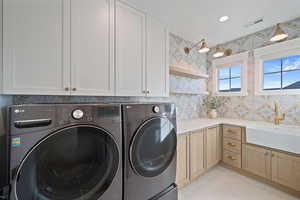 Clothes washing area featuring sink, washer and clothes dryer, and cabinets