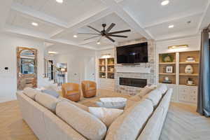 Living room featuring built in features, a fireplace, beamed ceiling, light parquet floors, and ceiling fan