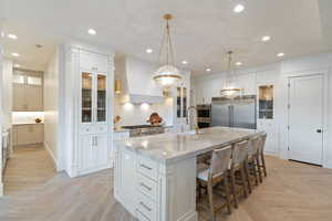 Kitchen with sink, custom exhaust hood, light parquet floors, a large island, and stainless steel appliances