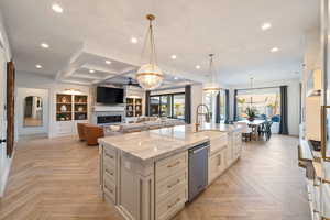 Kitchen featuring dishwasher, light parquet flooring, a kitchen island with sink, and decorative light fixtures