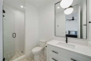 Bathroom with walk in shower, ceiling fan, vanity, and toilet