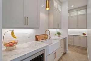 Kitchen with sink, light wood-type flooring, white cabinets, light stone countertops, and backsplash