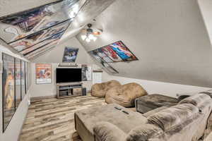 Living room with lofted ceiling, ceiling fan, light hardwood / wood-style flooring, and a textured ceiling