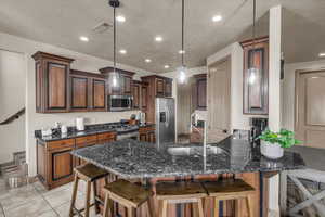 Kitchen featuring sink, appliances with stainless steel finishes, dark stone countertops, hanging light fixtures, and a kitchen breakfast bar